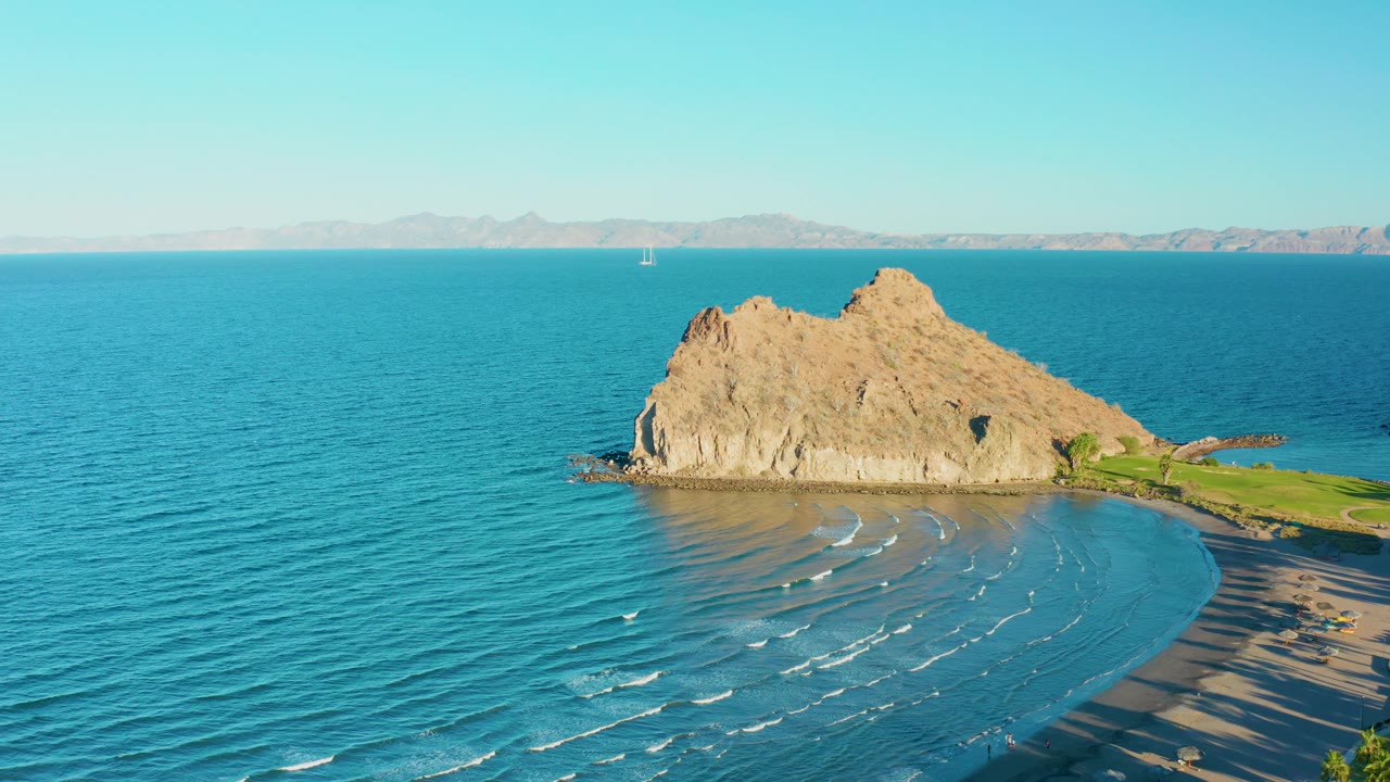 Loreto, Baja California Sur coastline seen from above with the rock formation slightly right of center, smooth blue water in front, distant land across the horizon, and no visible people.