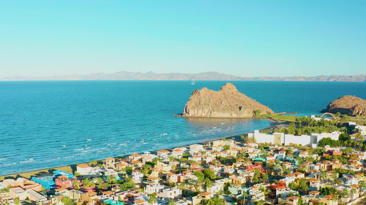 Wide coastal aerial with town, sea, and tan rocks