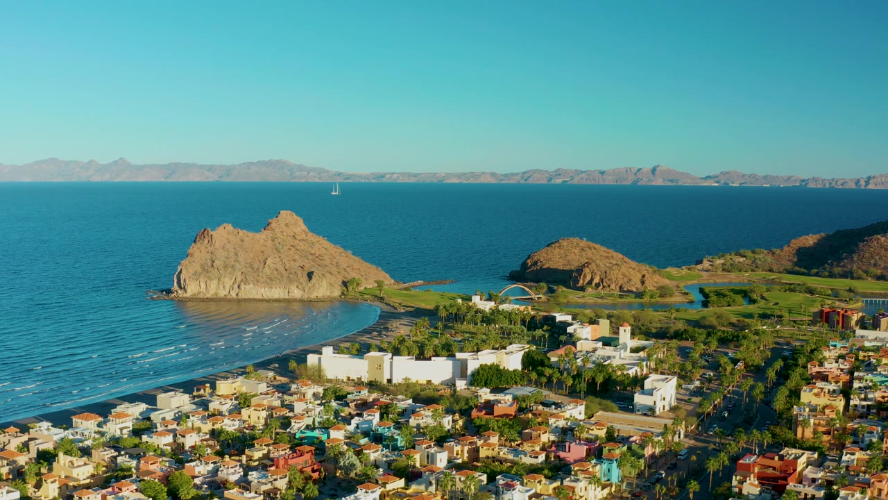 High aerial view of Loreto coastline with town foreground, resort buildings, bay, rock, and mountains.