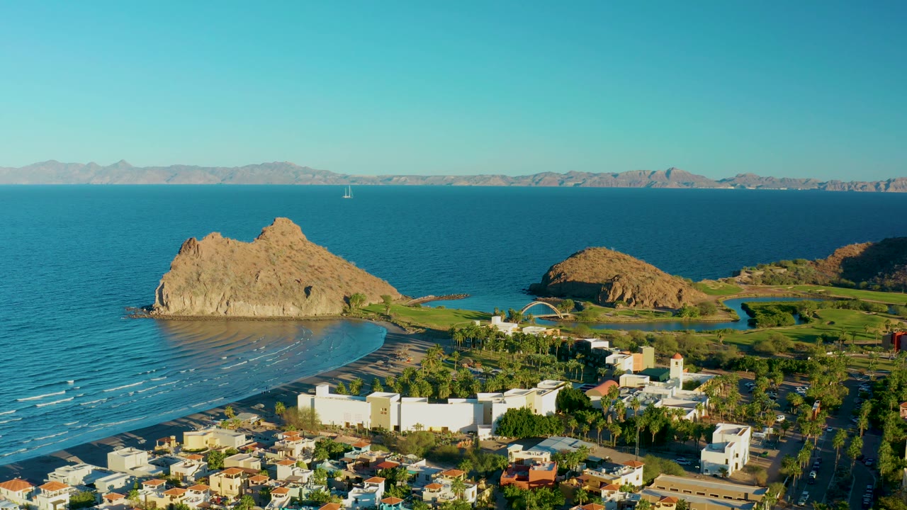 Aerial coastline view with town foreground, rocky headland, beach, and open water.