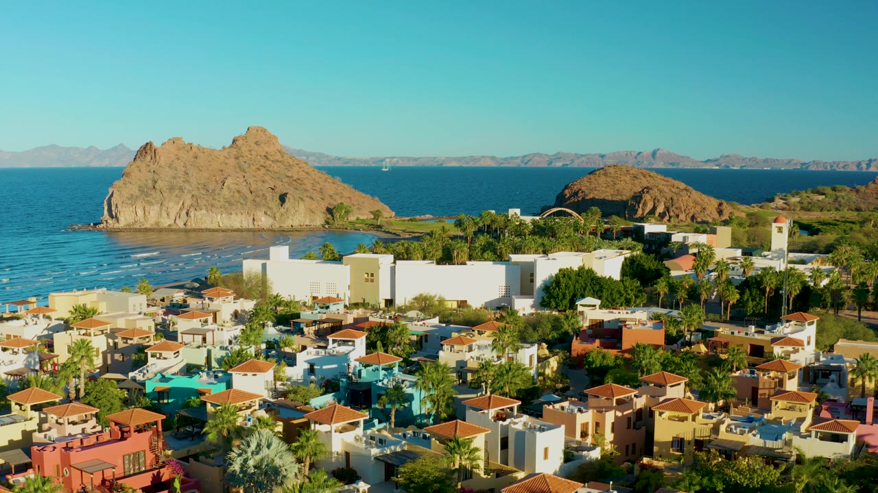 Aerial coastal neighborhood with colorful homes, palms, ocean, and rock formations.