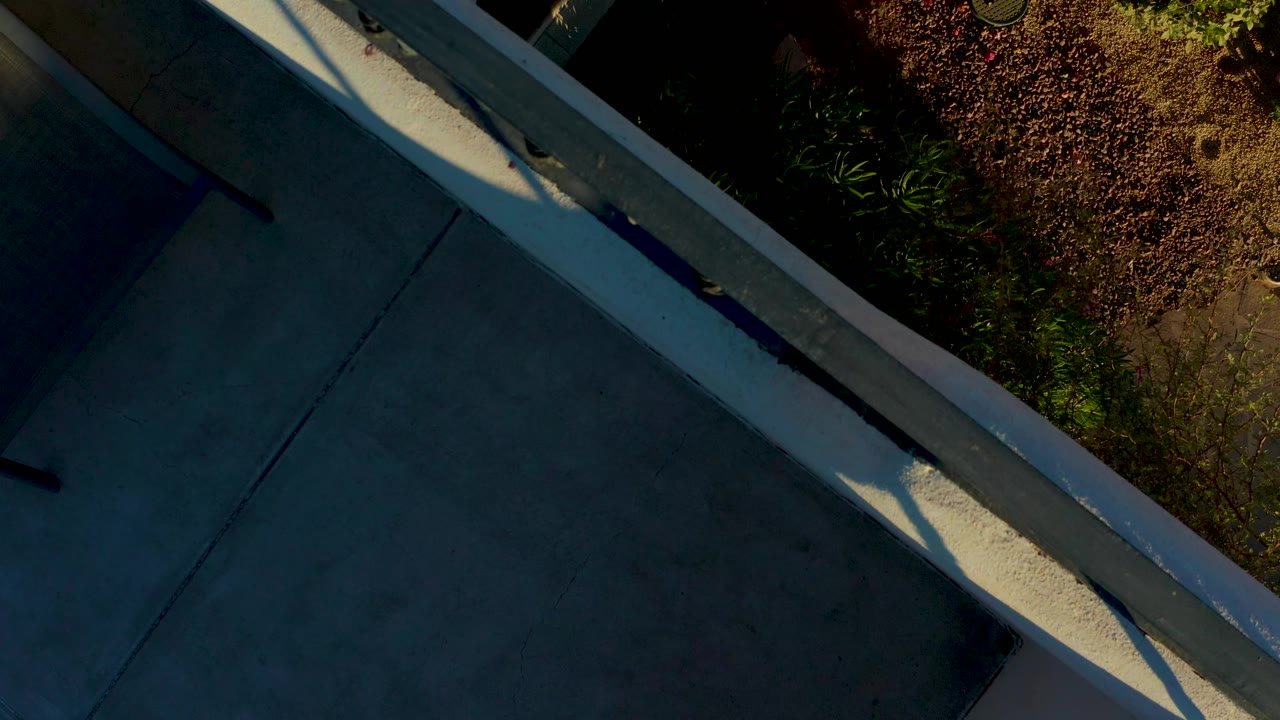 A similar overhead Loreto view holds on the concrete ledge and railing, with shaded pavement below, reddish planting to the side, and no visible people.
