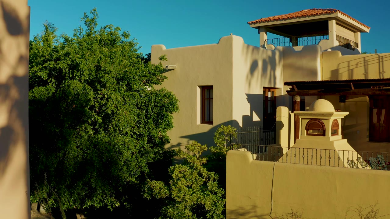 Adobe-style building with tree and balcony in bright sun
