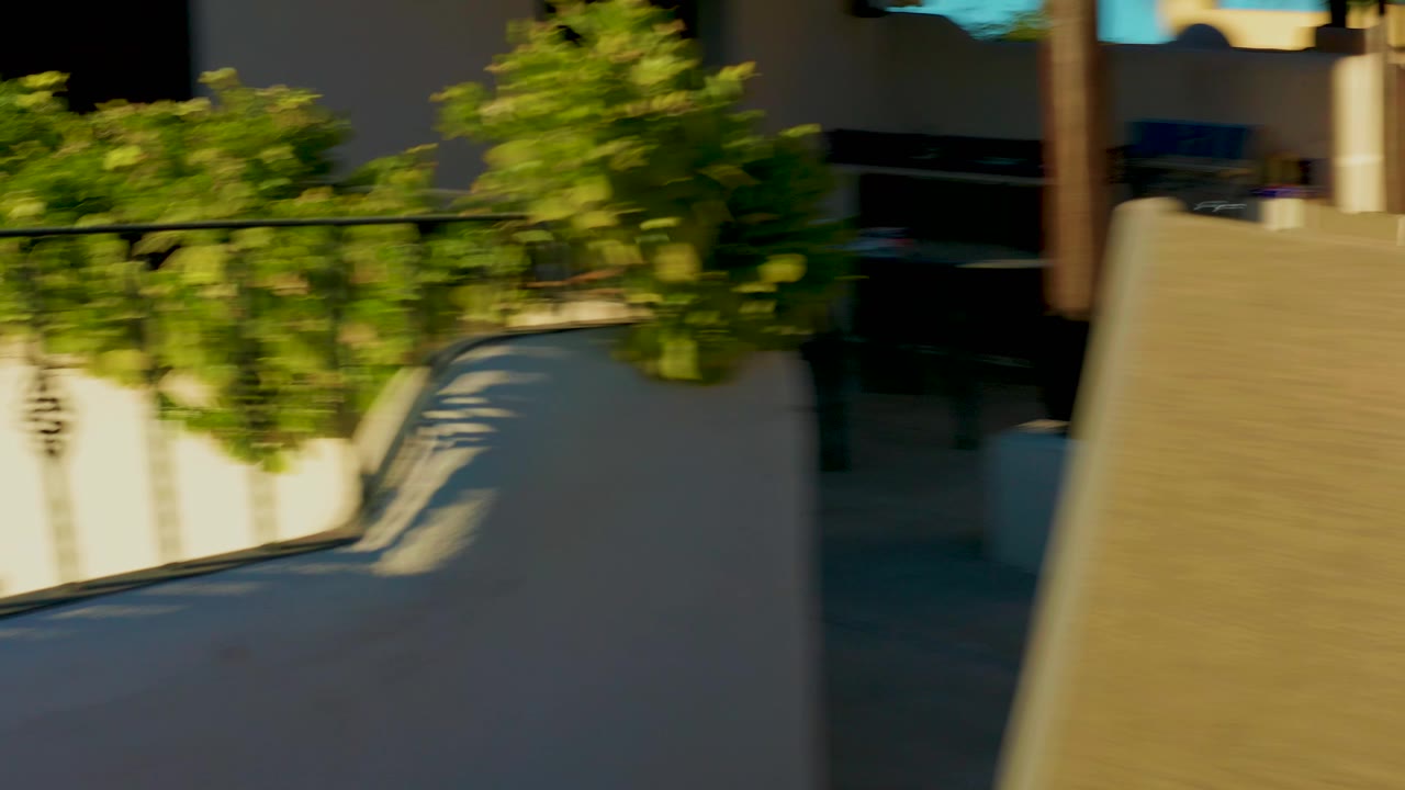 A white stucco courtyard wall, balcony or terrace edge, leafy tree, and shaded architectural openings appear in Loreto, Baja California Sur, with no visible people.