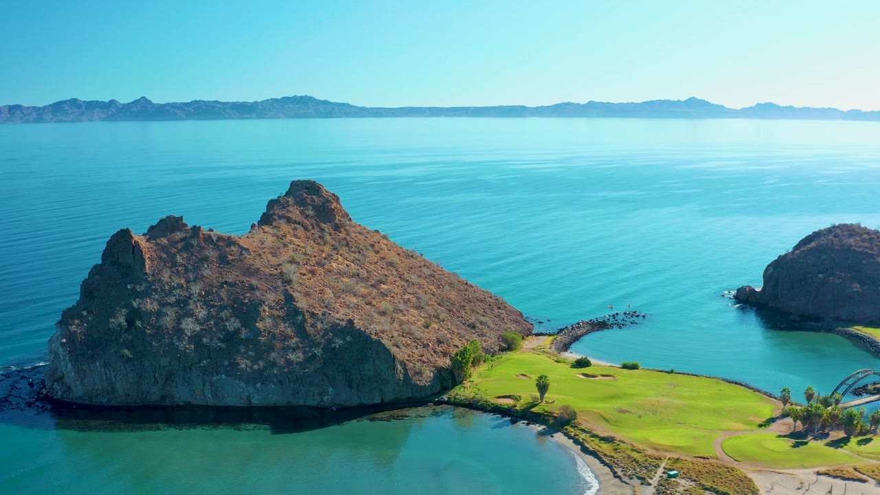 A high view over a rocky headland and green shoreline in Loreto, Baja California Sur, with calm blue water and distant hills, no visible people.