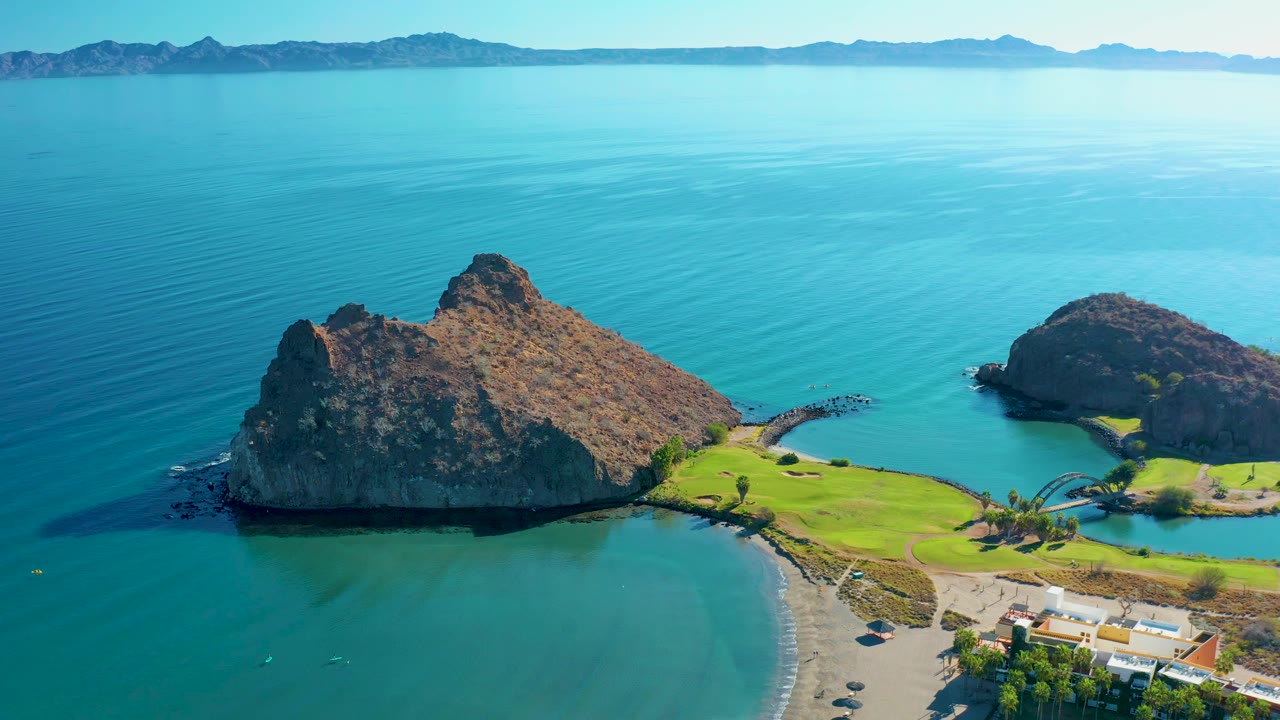 Drone view of two rocky outcrops beside a sandy beach and bright blue sea.