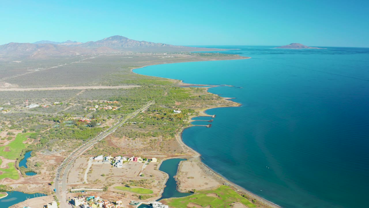 Elevated view of shoreline, coastal road, buildings, lagoons, and blue water.