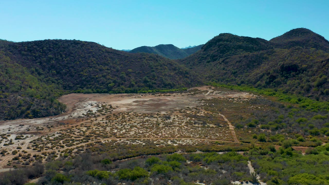 Dry basin with scattered shrubs and dark green hills beyond.