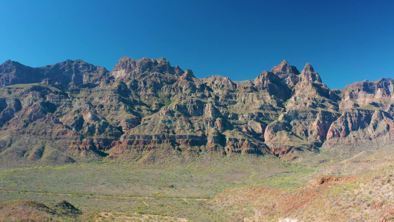 Desert foreground leading to layered mountains beneath cloudless sky.