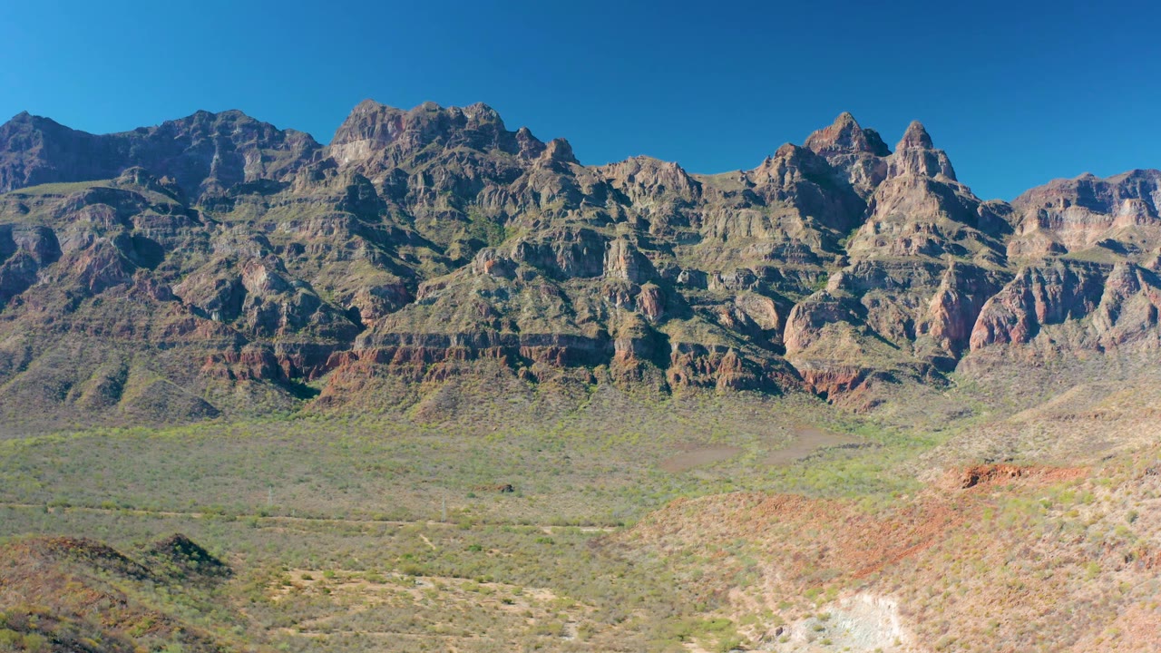 Mid-clip view in Loreto, Baja California Sur showing a broad arid valley, low green scrub, striated mountain faces, and no visible people.