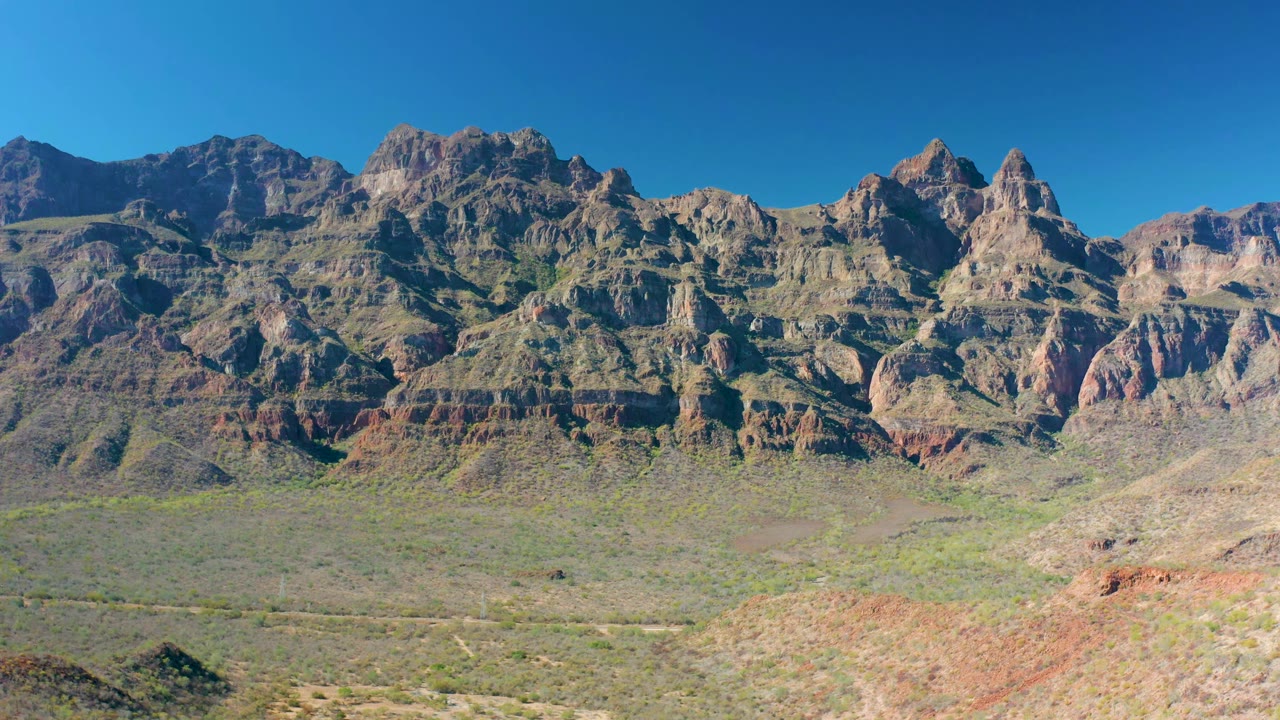 Second frame shows the Loreto mountain ridge slightly farther along the view, with gray and reddish rock layers above dry green valley scrub and no visible people.