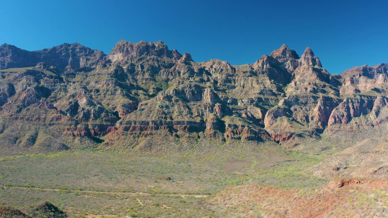 Fourth frame presents the rugged Loreto mountain wall across the horizon, with sunlit tan rock, darker shadowed slopes, dry valley scrub, and no visible people.