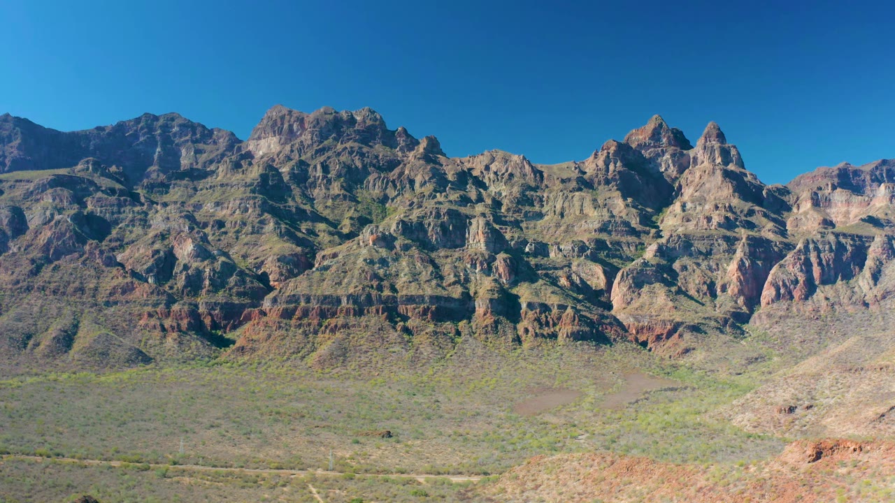 The Loreto mountain ridge fills the frame with visible red and brown strata, sparse desert vegetation, and no visible people.