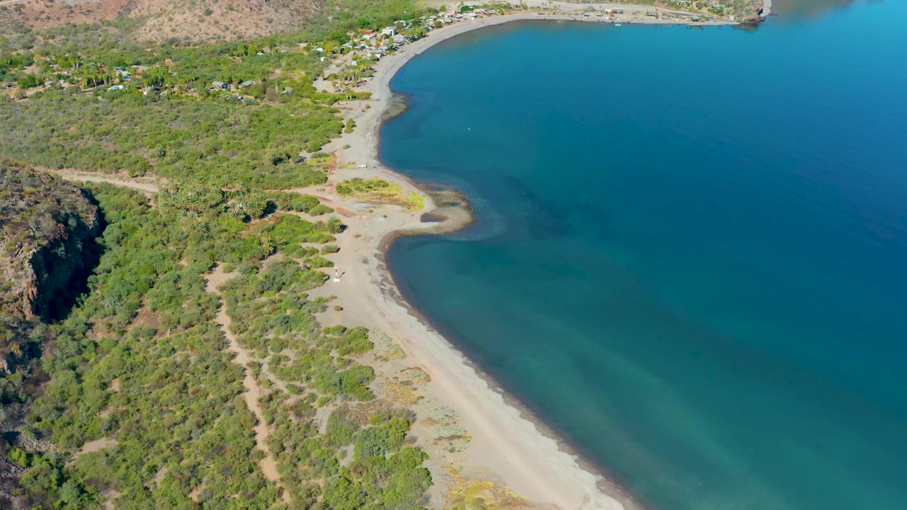 Elevated view of a sandy shoreline curving around clear blue-green water.