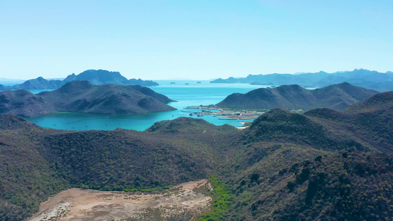 Aerial view in Juncalito, Baja California Sur with rounded hills crossing the foreground, blue-green water behind them, distant mountainous islands, and no visible people.