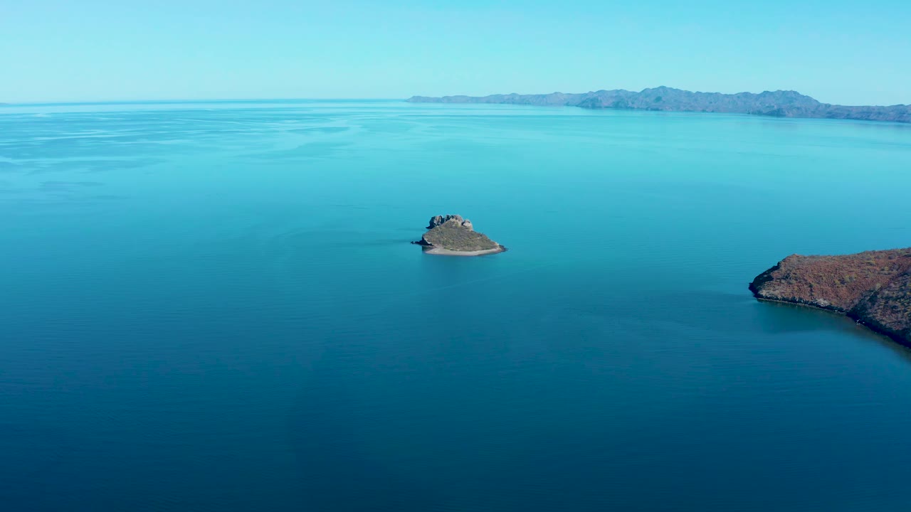 Aerial frame over Juncalito water with the small island left of center, the larger rocky landmass at the right edge, distant mountains, and no visible people.