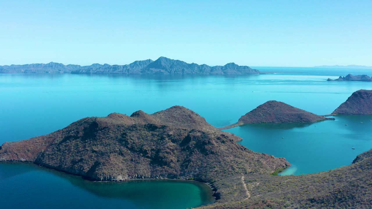 Rocky islands surrounded by turquoise water with distant mountains and blue sky.