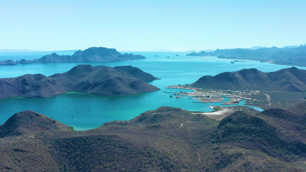 A second aerial frame of Juncalito shows the cove centered below rounded mountain ridges, with small boats in the water and no visible people.