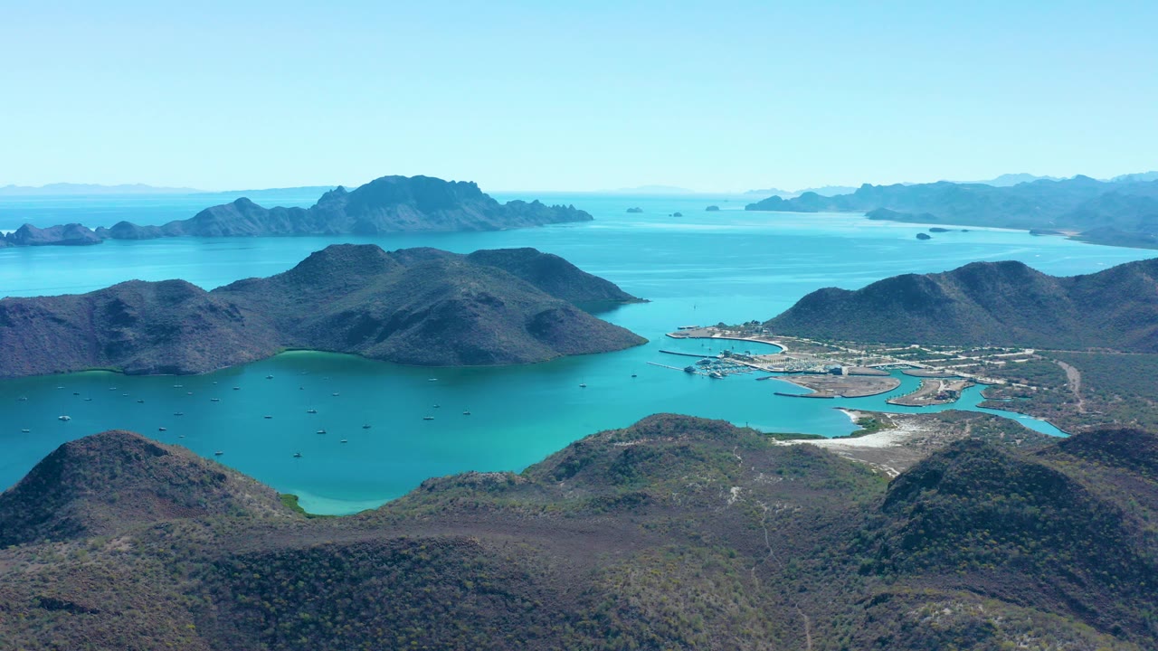Aerial view of turquoise bay, rolling hills, distant islands, and shoreline structures.