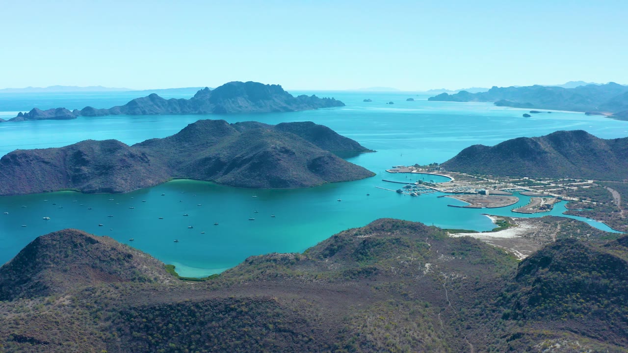 Aerial view of turquoise bay, rocky hills, islands, and scattered boats.