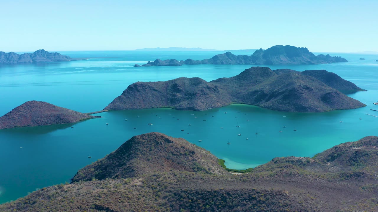 Elevated view in Juncalito showing barren rocky islands across calm turquoise water, small boats between the islands, layered distant landforms, and no visible people.