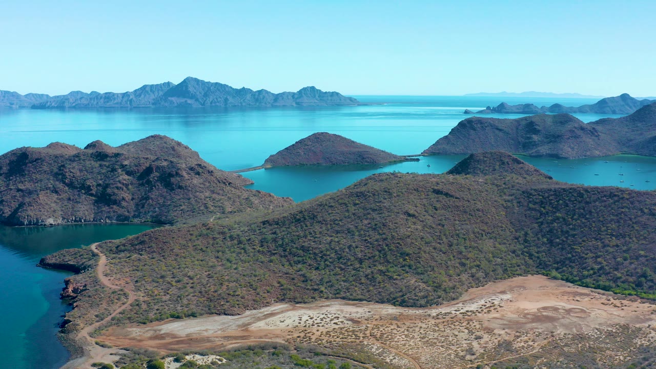 Aerial view of coastal hills, turquoise bays, and distant mountains.
