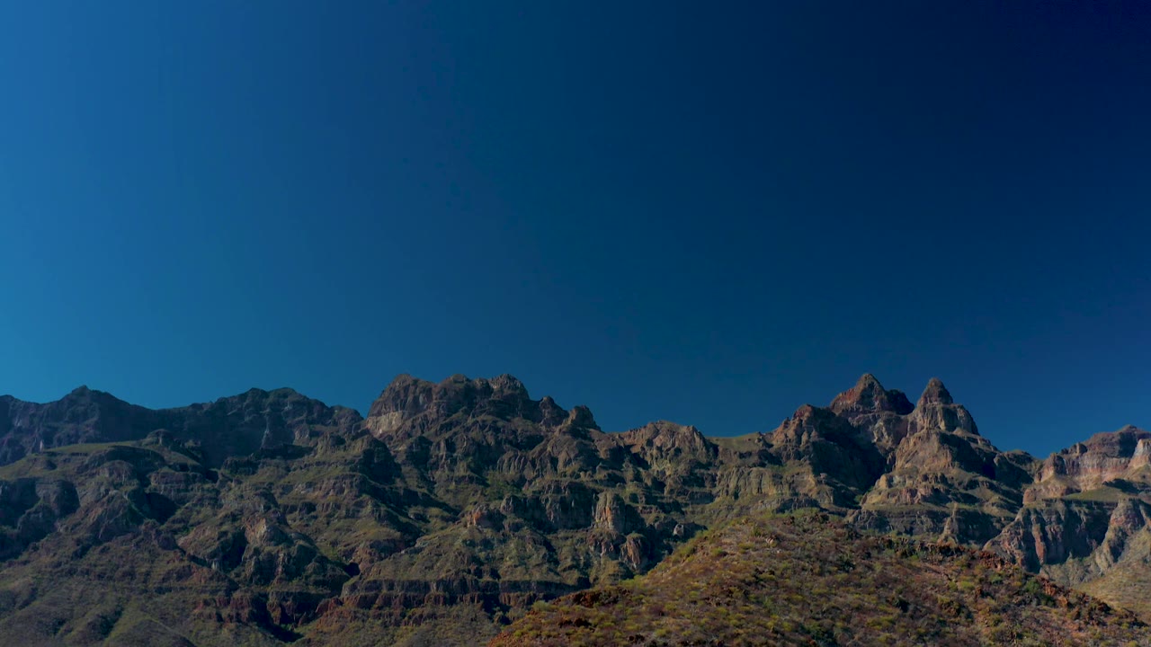 Clearer view of rugged layered mountain peaks near Juncalito, Baja California Sur, with a scrub-covered hill in front and no visible people.