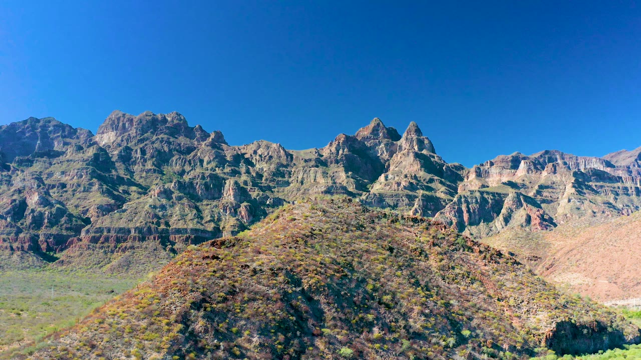 Mountain range and scrubby foreground hill in bright daylight.