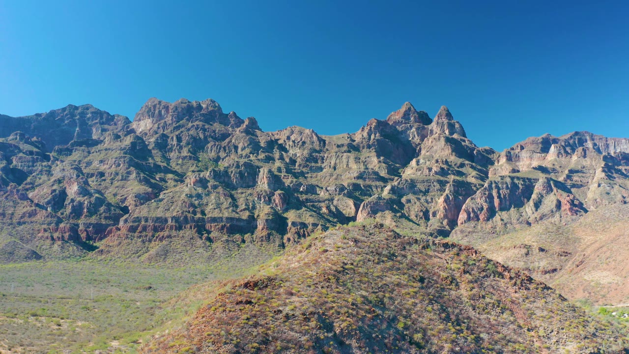 Wide view near Juncalito with jagged mountain peaks, pale desert slopes, sparse green scrub, and no visible people.