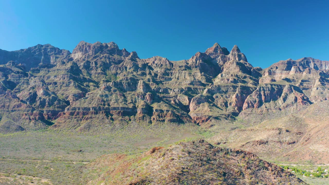 Early frame of the Juncalito mountain landscape showing jagged layered peaks, muted red rock bands, a scrub-covered valley, and no visible people.