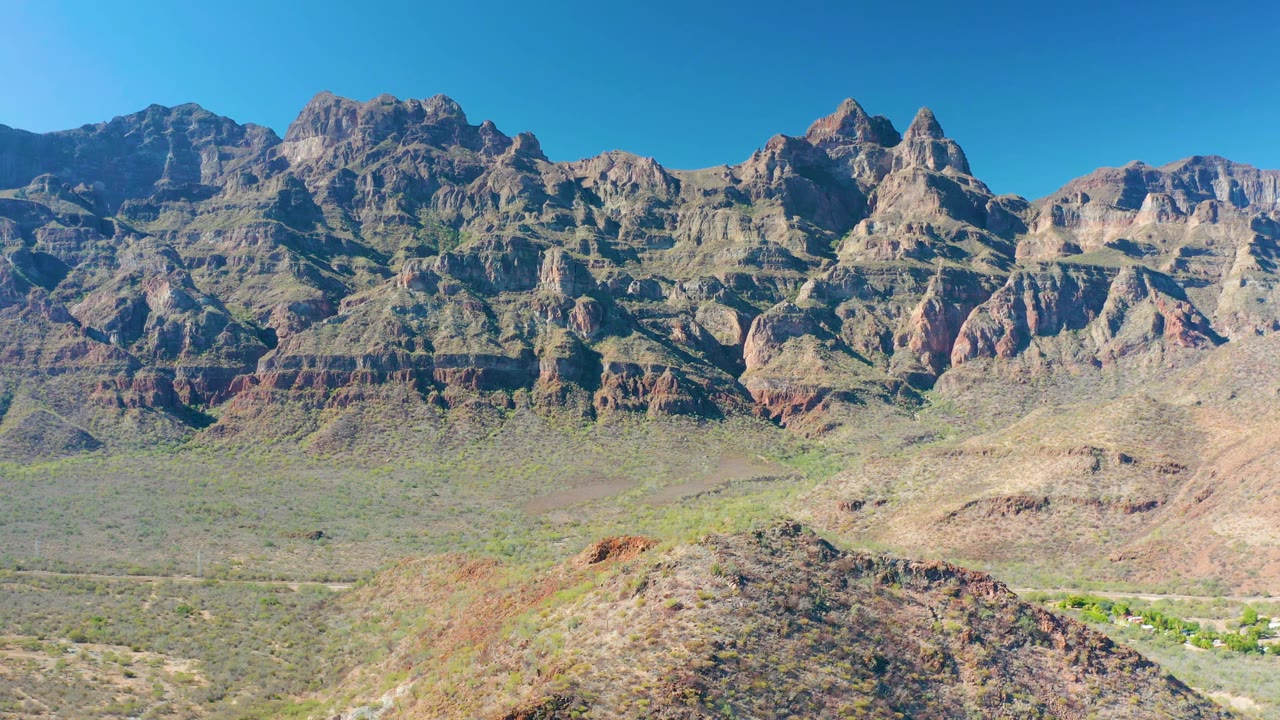 Juncalito mountain range seen across a pale desert valley, with reddish rock bands, scrub vegetation, a foreground hill, and no visible people.