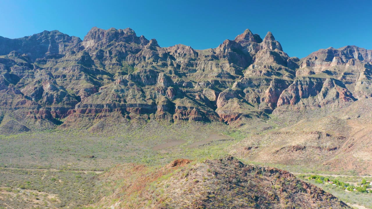 Jagged peaks and layered rock faces near Juncalito rise above a dry valley, with a low sloping ridge in front and no visible people.