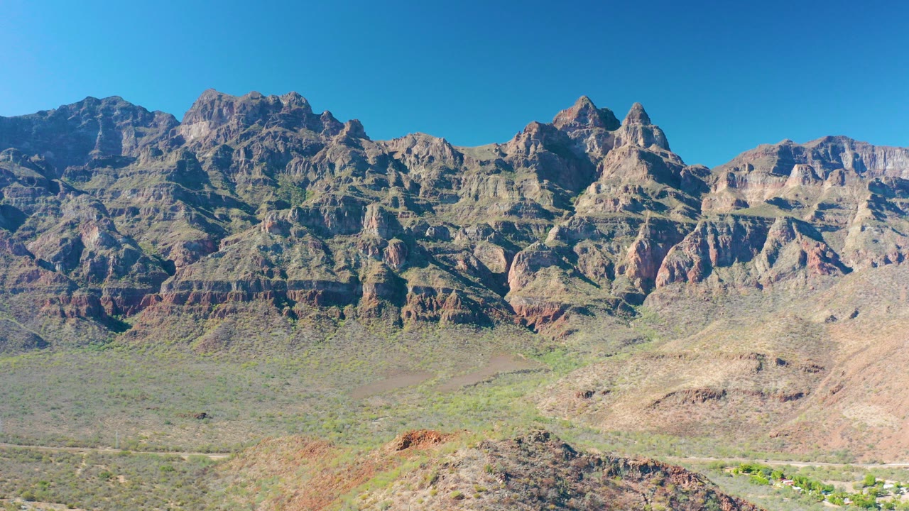 Opening frame of a Juncalito, Baja California Sur mountain range with layered rock faces, sparse desert vegetation, a pale foreground outcrop, and no visible people.