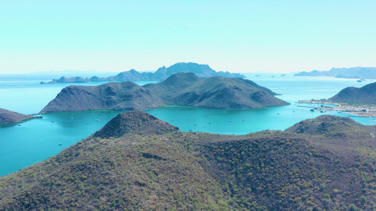 Aerial view of scrub hills, turquoise water, islands, and distant settlement