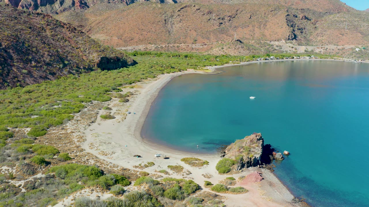 Wide aerial view of a sandy cove bordered by vegetation and rocky hills.