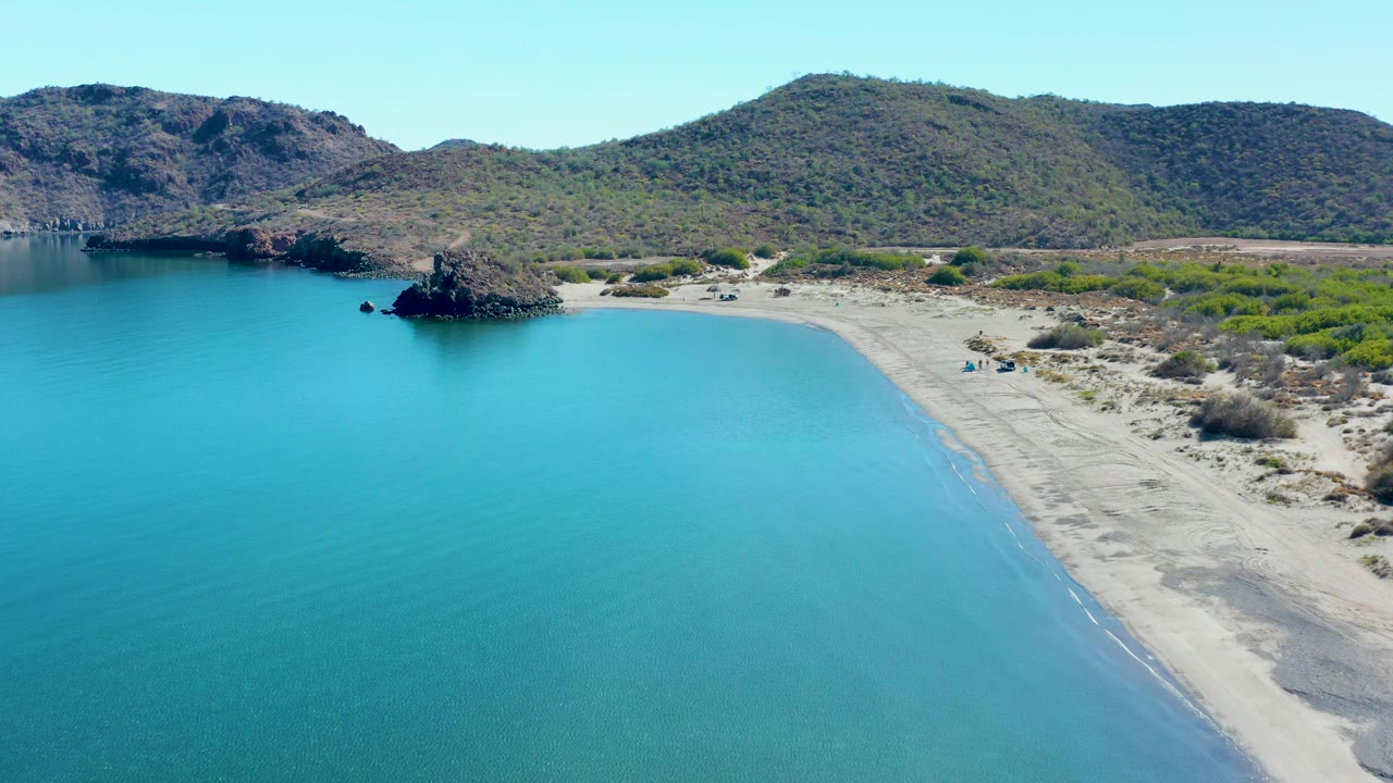 Aerial cove view with turquoise water and rocky shoreline below hills.