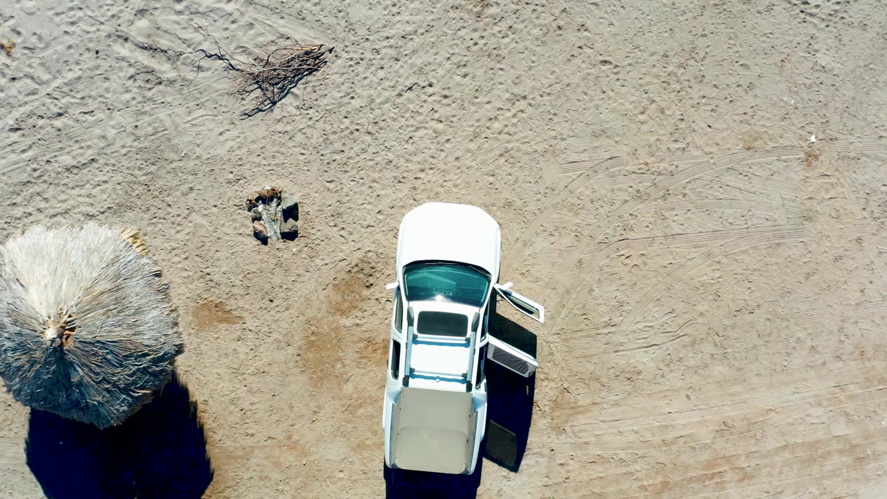 Juncalito overhead view where the thatched umbrella sits near the lower left and the white car with an open door remains on the right, with no visible people.