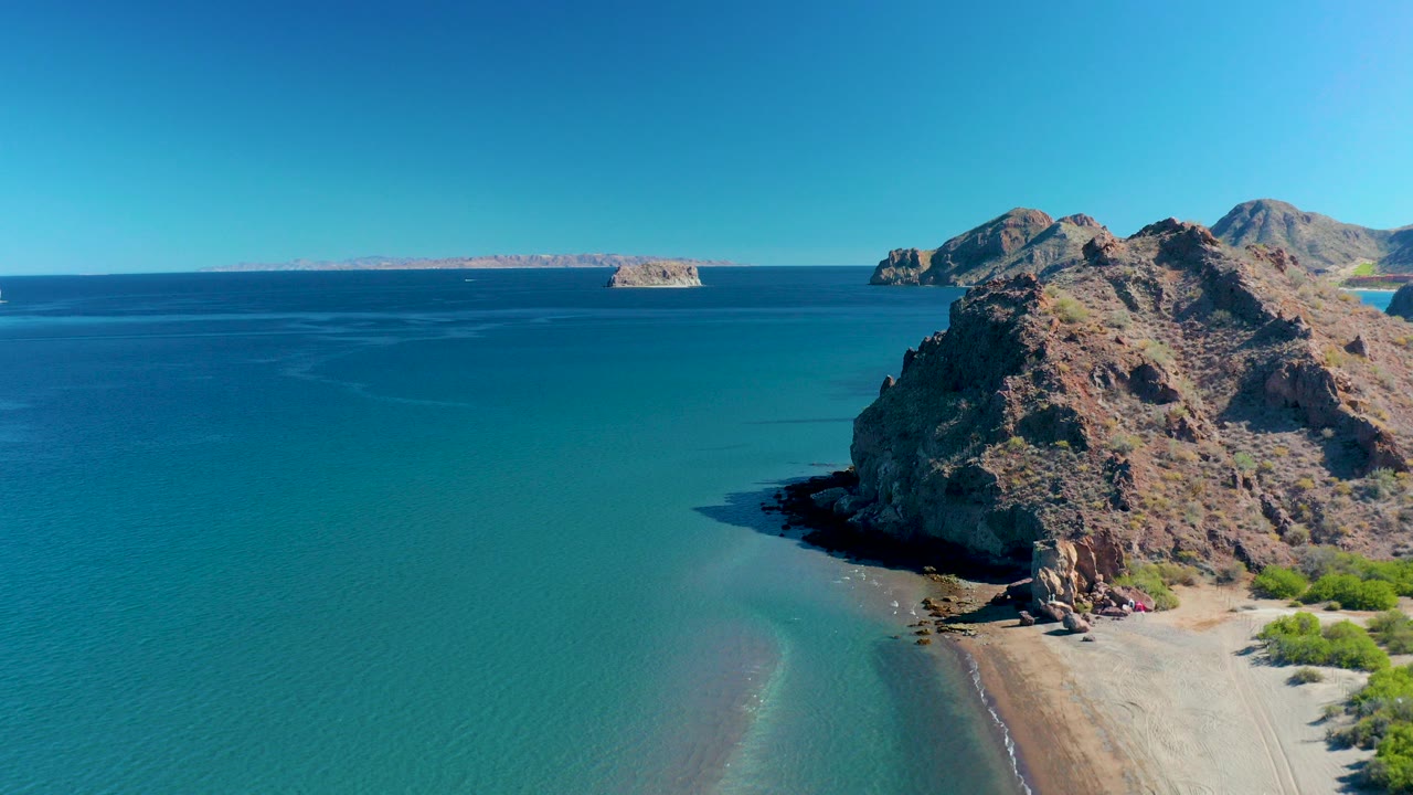 Aerial view of rocky coast, turquoise water, sandy beach, and distant islands.