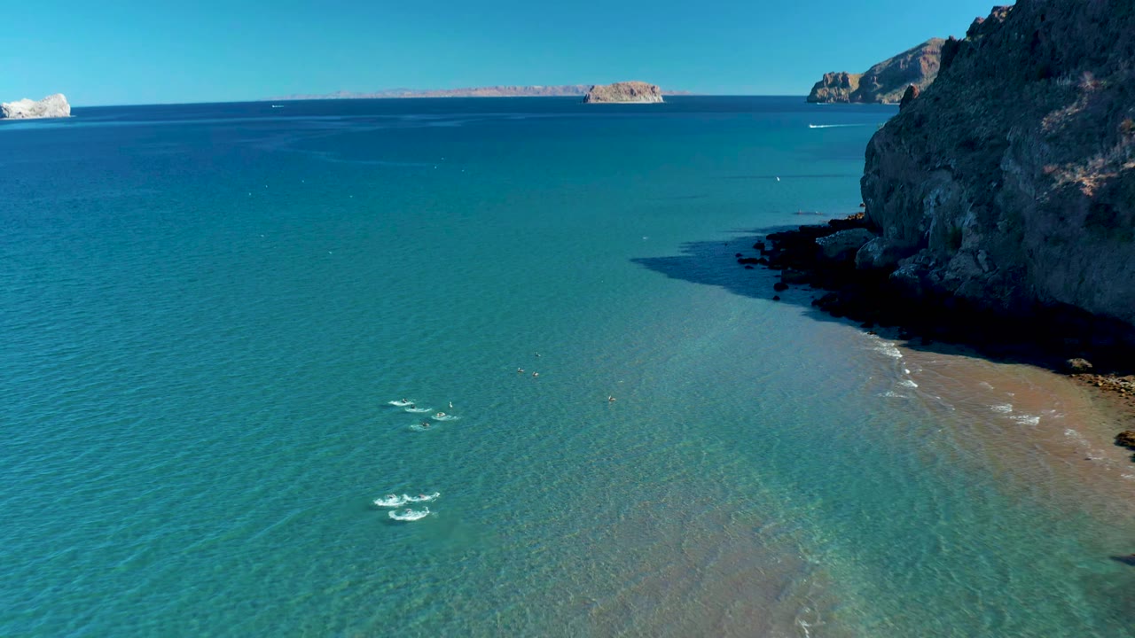 Clear blue ocean with small swimmers near a rocky coast.