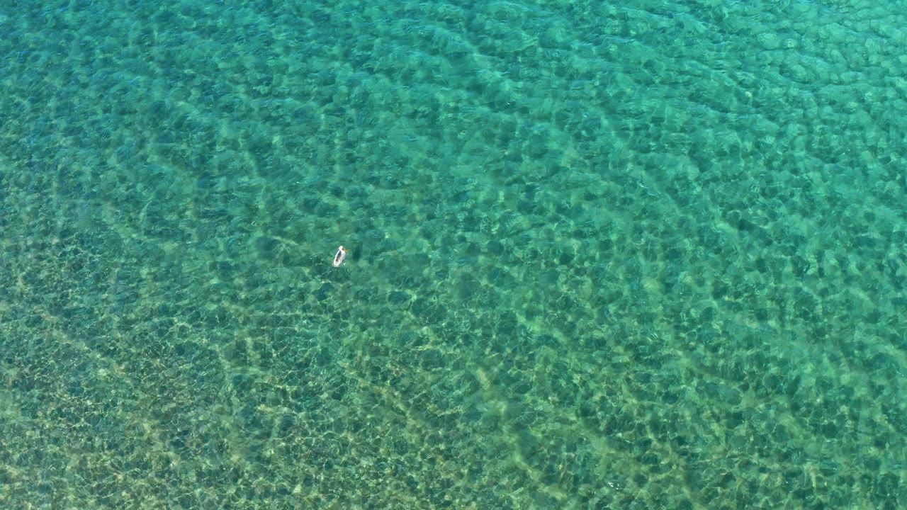 Clear shallow water with a small swimmer near the center.