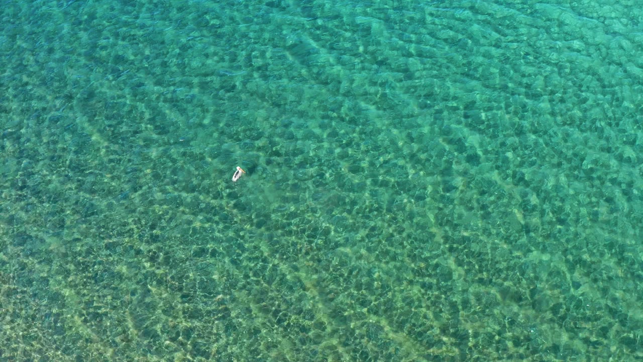 Overhead shallow sea with one small swimmer toward the left.