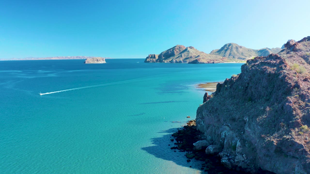 Small boat crossing turquoise water near rocky coast