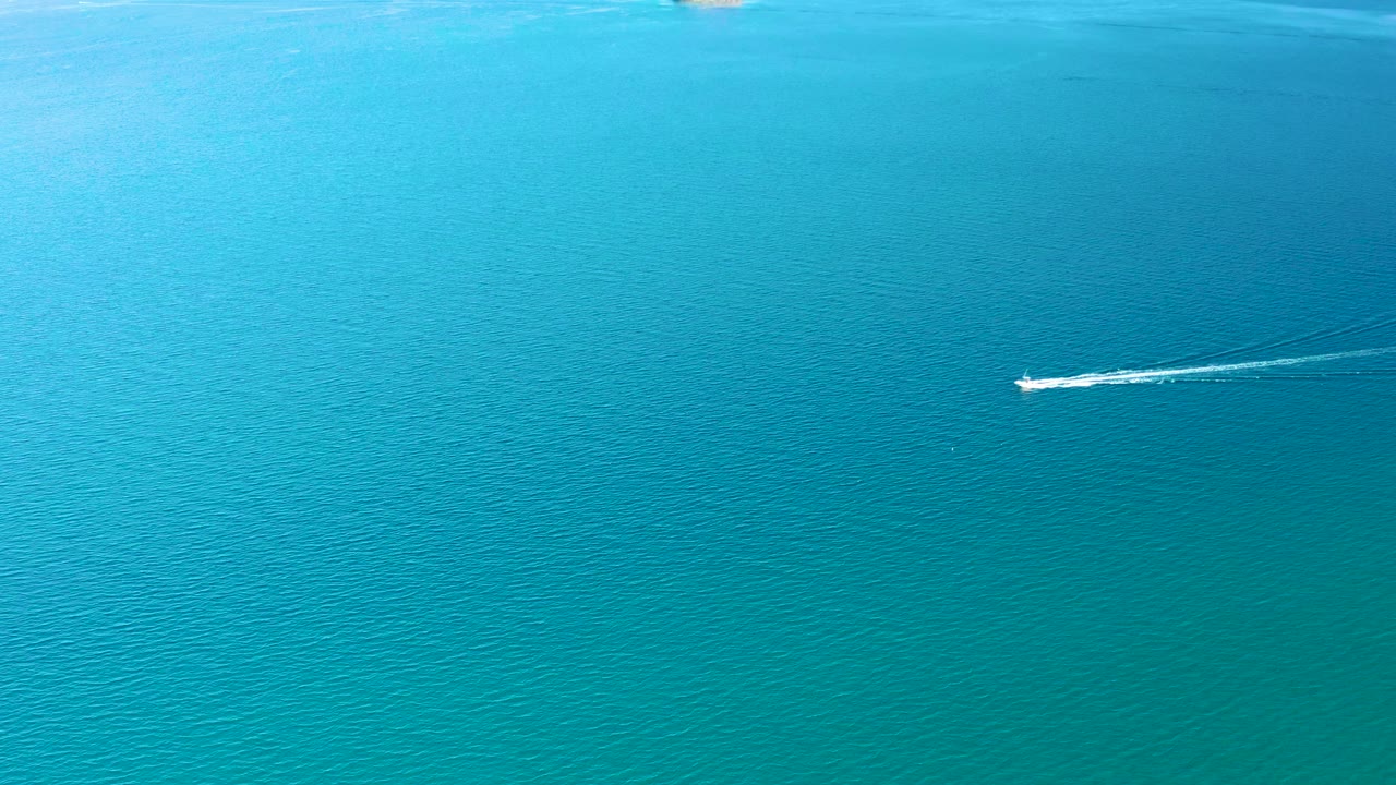 At 0:00 in Ligui, Baja California Sur, a small white boat appears high in the frame on turquoise ocean water with a thin wake behind it and no visible people.