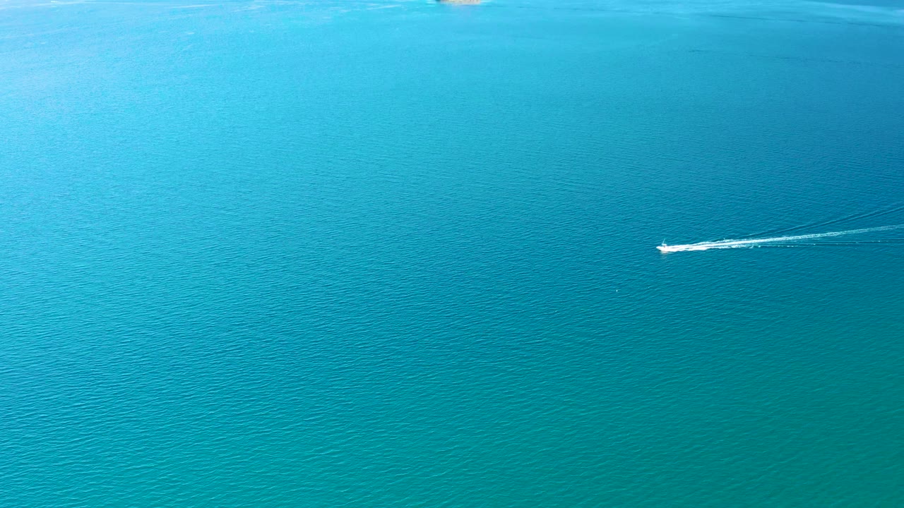 Small boat moving across blue-green ocean with a trailing wake.