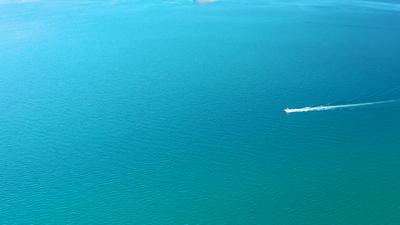 At 0:02 in Ligui, Baja California Sur, the small boat sits near the right side of the frame, pulling a bright wake across uninterrupted turquoise sea with no visible people.