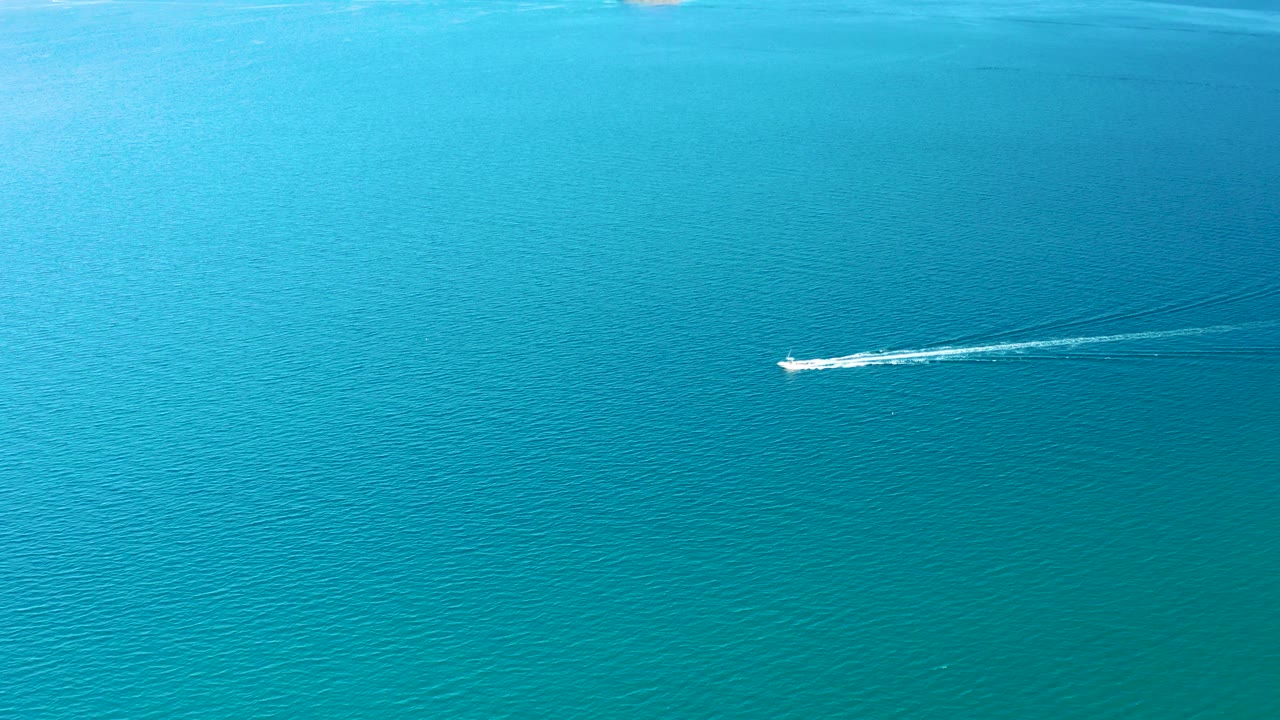 The boat has advanced across the calm turquoise water in Ligui, Baja California Sur, with its white wake extending farther behind and no visible people.