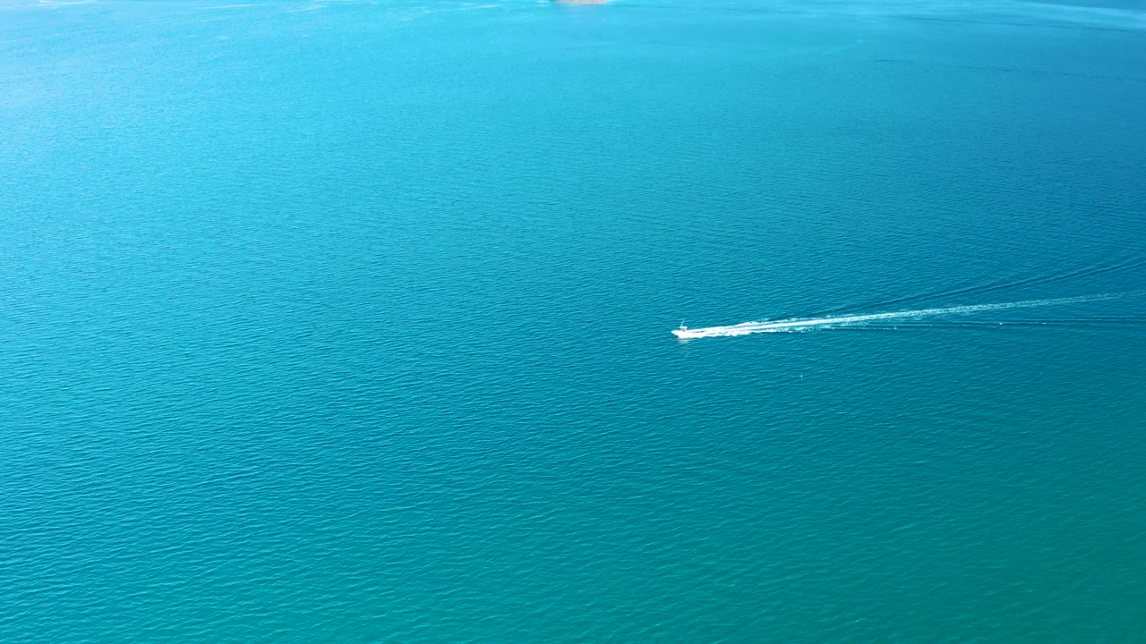 A small speedboat sits farther to the right over open turquoise ocean in Ligui, Baja California Sur, pulling a long white wake with no visible people.