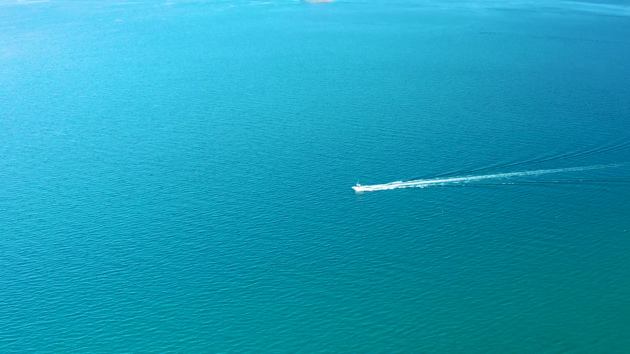 The white boat crosses open teal water in Ligui, Baja California Sur, with a diagonal wake line spreading behind it and no visible people.