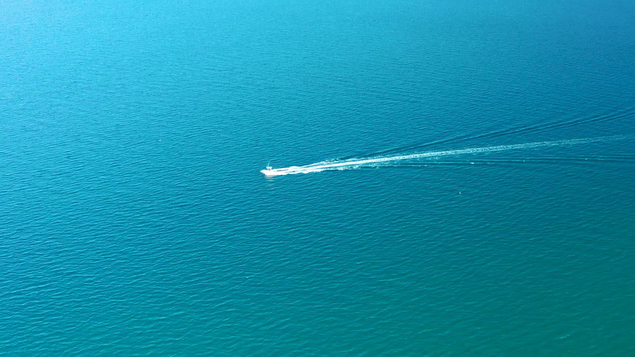 Small white speedboat crossing blue ocean with a white wake