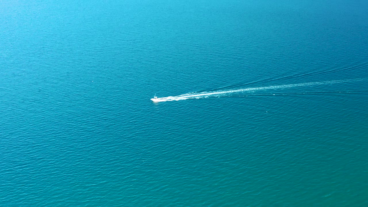 The white speedboat continues across turquoise ocean near Ligui, Baja California Sur, with its wake stretching longer across the rippled surface and no visible people.